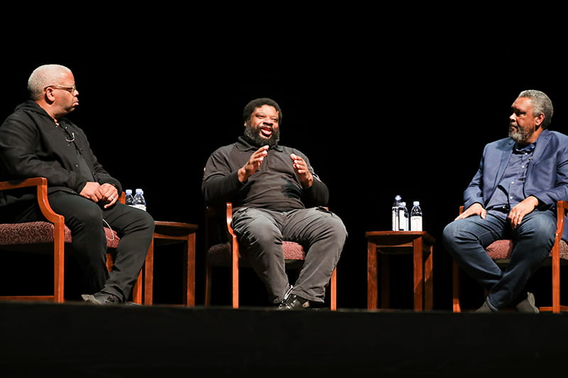 3 Men seated on an auditorium stage