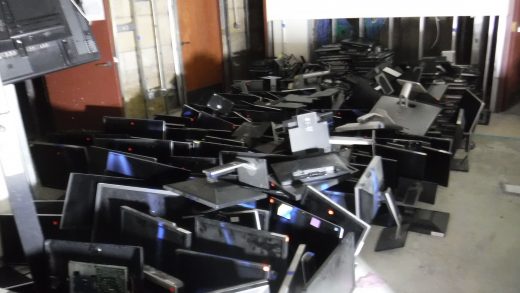 Dozens of computer screens sit on a concrete floor.