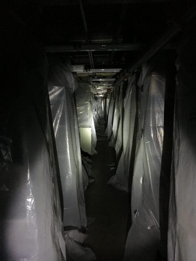 Rows of metal shelving draped in plastic are lit up by a flashlight.