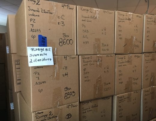 Large cardboard boxes marked with call number ranges, shelf rows and ranges are stacked three high and four across. 