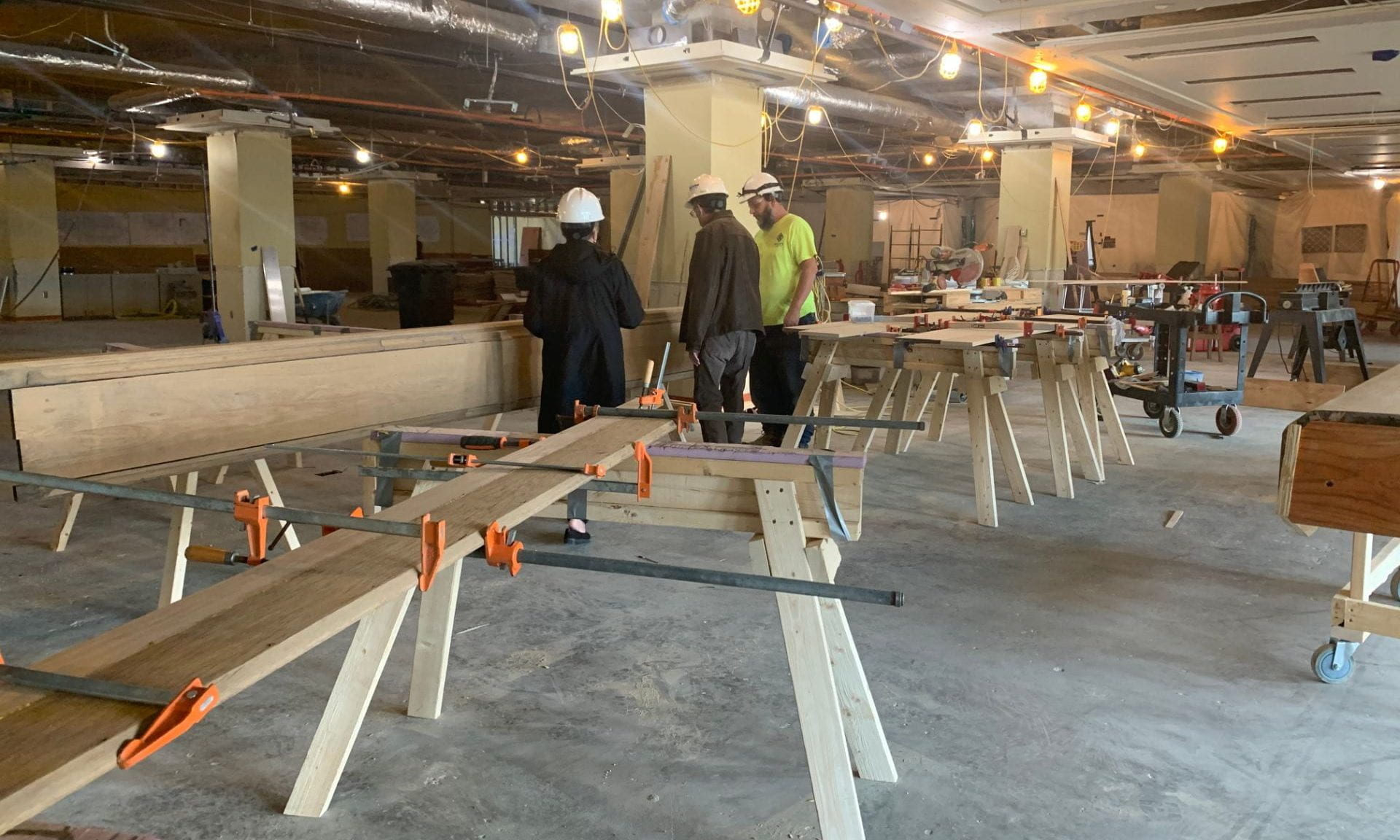 Dean of Libraries, Lori Goetsch, and Associate Dean, Mike Haddock, talk with a worker. They are surrounded by wood in various stages of repair.