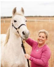 Woman in pink shirt holding reins of a white horse
