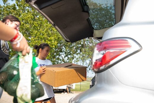 Volunteers place boxed food into a vehicle trunk